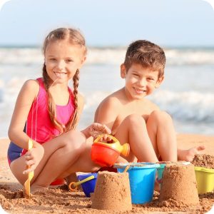 two kids building sand castles at the beach. Download our summer packing list for the beach