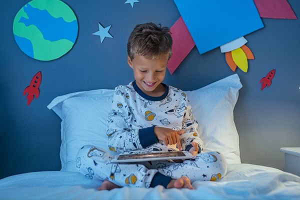 Boy on his bed watching something on a tablet at night